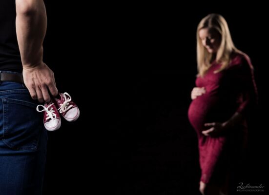Babyschuhe im Vordergrund bei Babybauch Shooting Der Fotograf setzt die Babyschuhe ins Licht, bei einem Schwangerschafts Fotohooting in Bonn